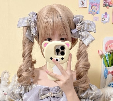A person taking a mirror selfie wearing a blonde double-pigtail wig with large gray bows, a lavender-gray bow-embroidered dress, and holding a cream-colored phone with a bear-shaped case.