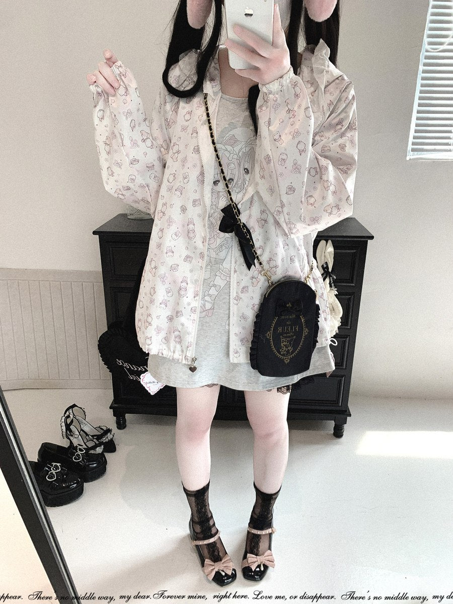 A person takes a mirror selfie showing a fashion outfit consisting of a sheer white long-sleeve jacket with a pink floral pattern, a light gray dress, black lace-up ankle socks, and black platform sandals with pink bows. A small black crossbody bag with gold lettering is also visible.