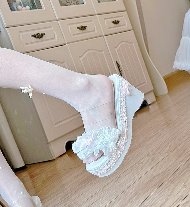 White sandals with lace details worn indoors on a wooden floor.
