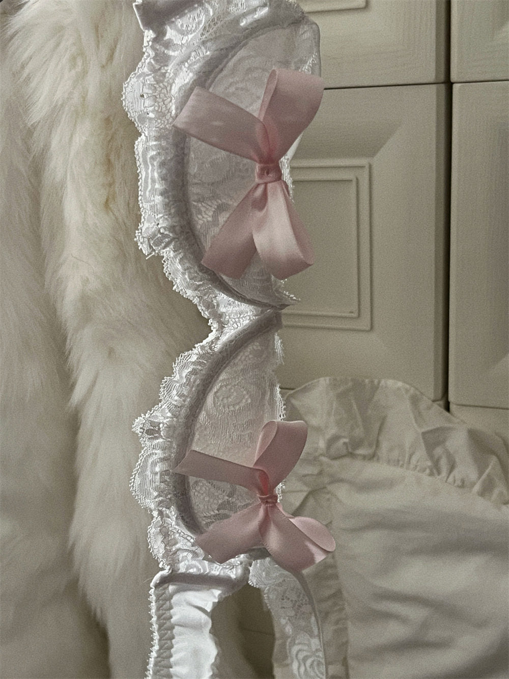 Decorative headboard with lace details and pink bows against a neutral wall.