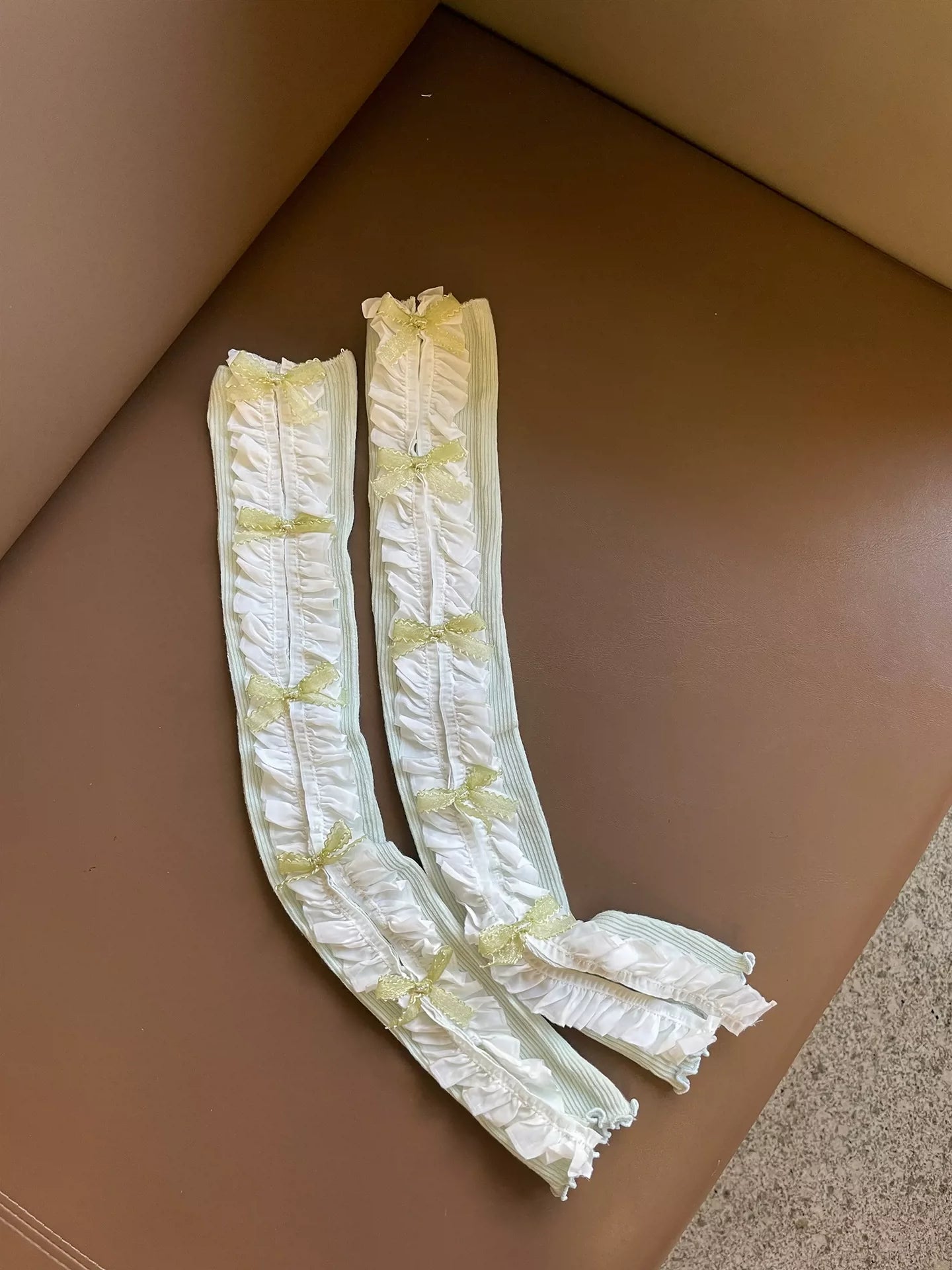 Two white lace arm warmers with decorative elements on a brown surface.