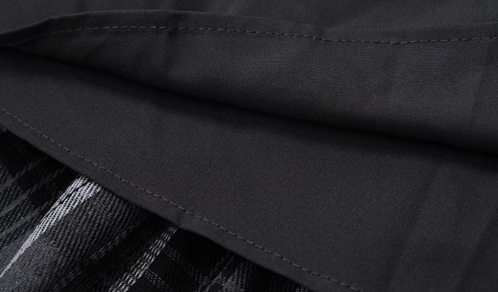 Close-up of a black fabric garment with visible stitching, showing part of a black-and-white plaid pattern underneath.