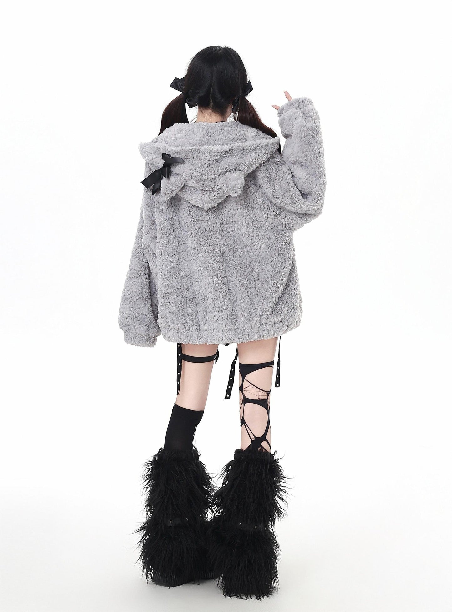 Person wearing a gray fluffy coat with a hood and black feathered boots on a white background