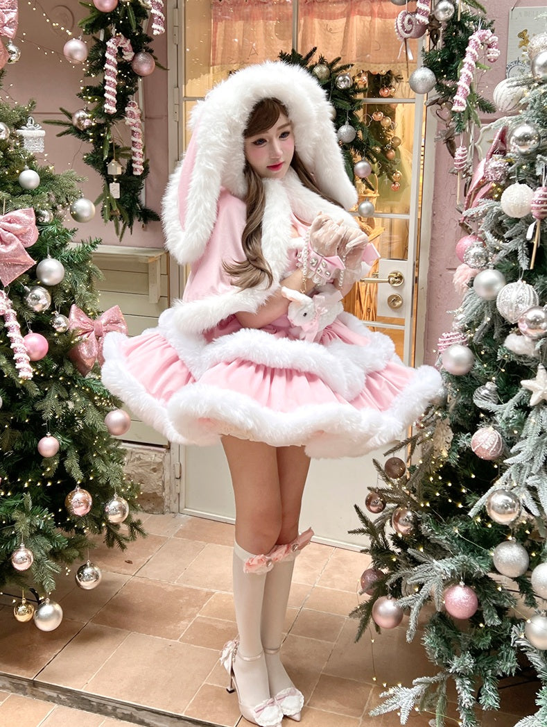 Person in a pink and white festive outfit standing between two decorated Christmas trees.
