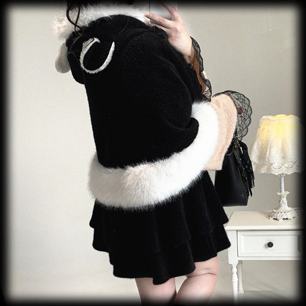 Person wearing a black outfit with white fur trim in a room setting.