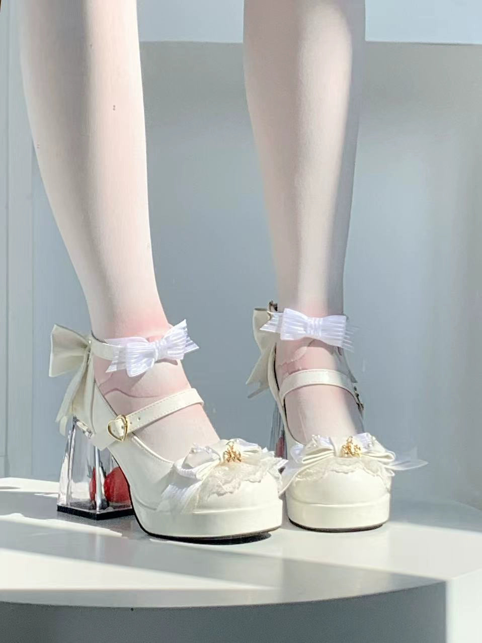 White high-heeled shoes with bow details on a white platform.