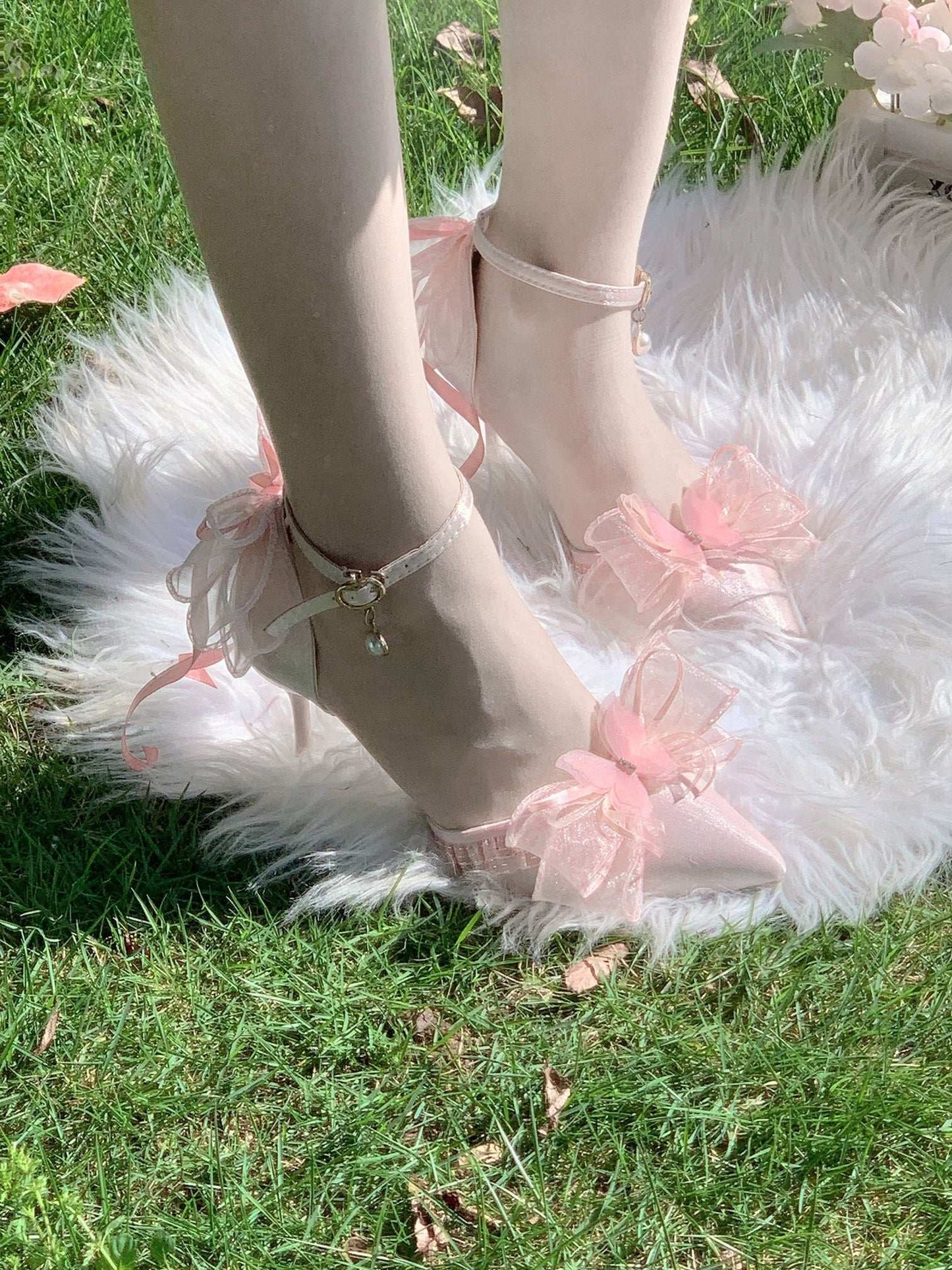 Pink ballet shoes with ruffles on a fluffy white rug and grass background