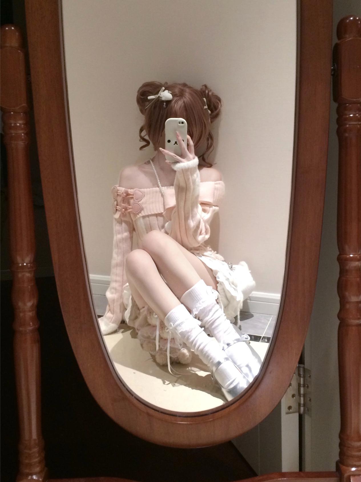 Person taking a mirror selfie wearing a pink dress and white boots in a room with wooden furniture.