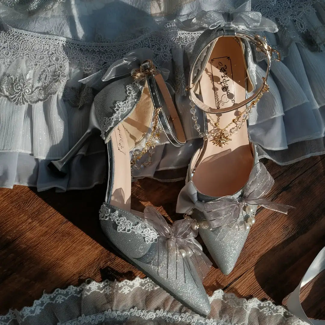 Pair of silver high-heeled shoes with decorative ribbons on a wooden surface.