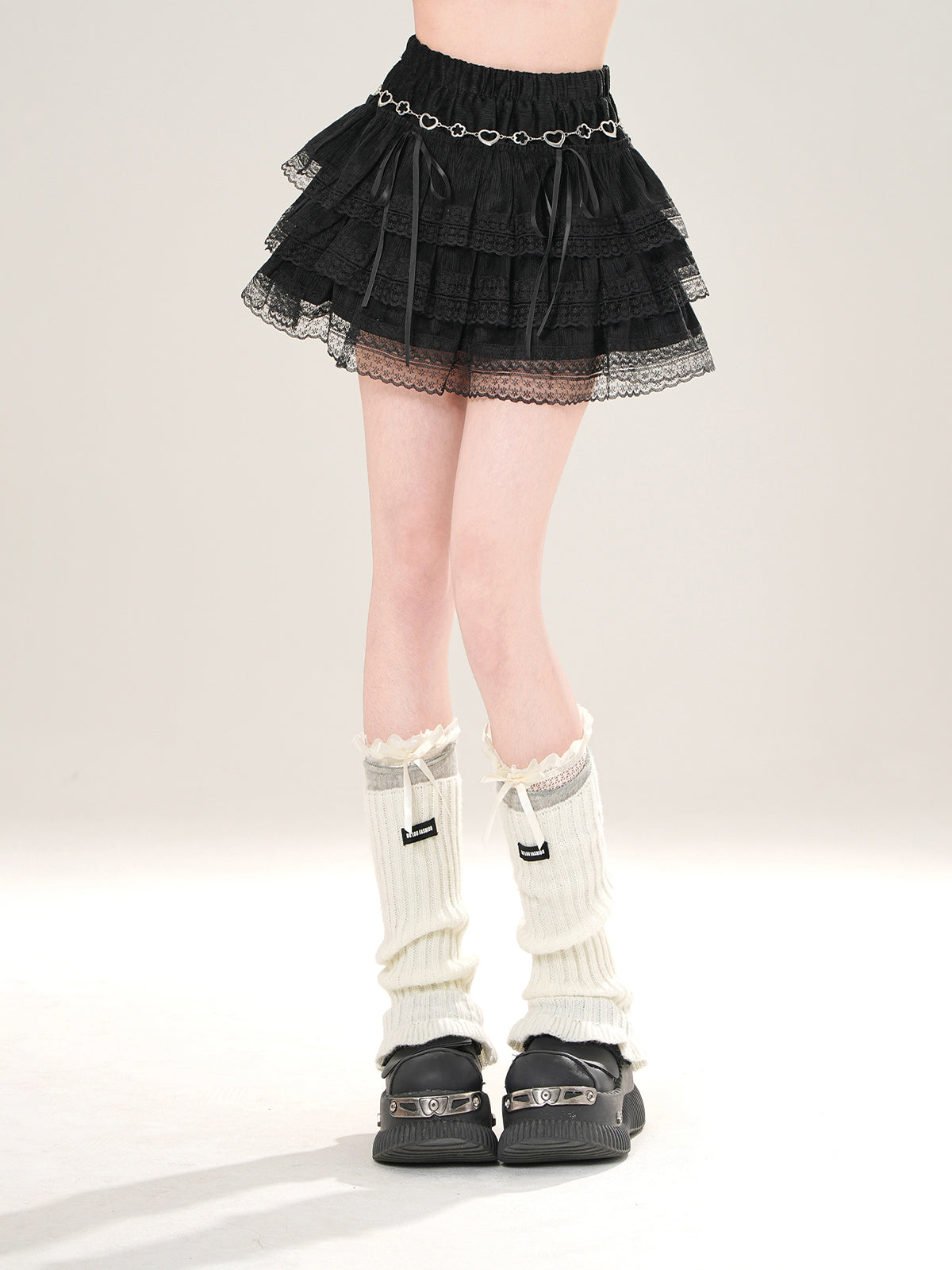 Person wearing a black tiered skirt, white knee-high socks, and black shoes on a light gray background