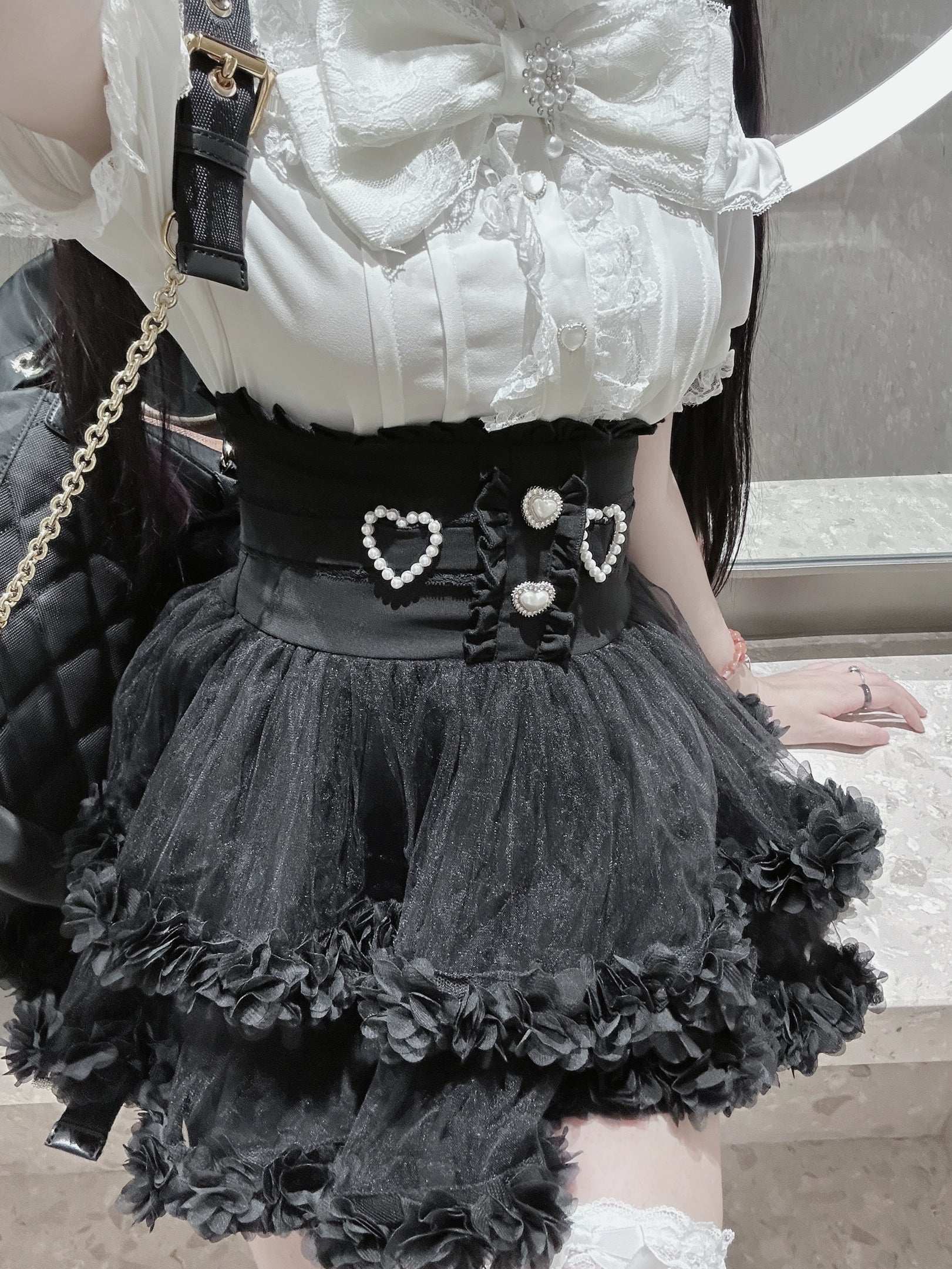 Person wearing a white lace top and black ruffled skirt with heart details.