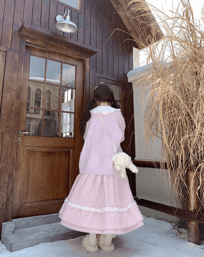 Person in a pink dress standing in front of a wooden door with snow on the ground.