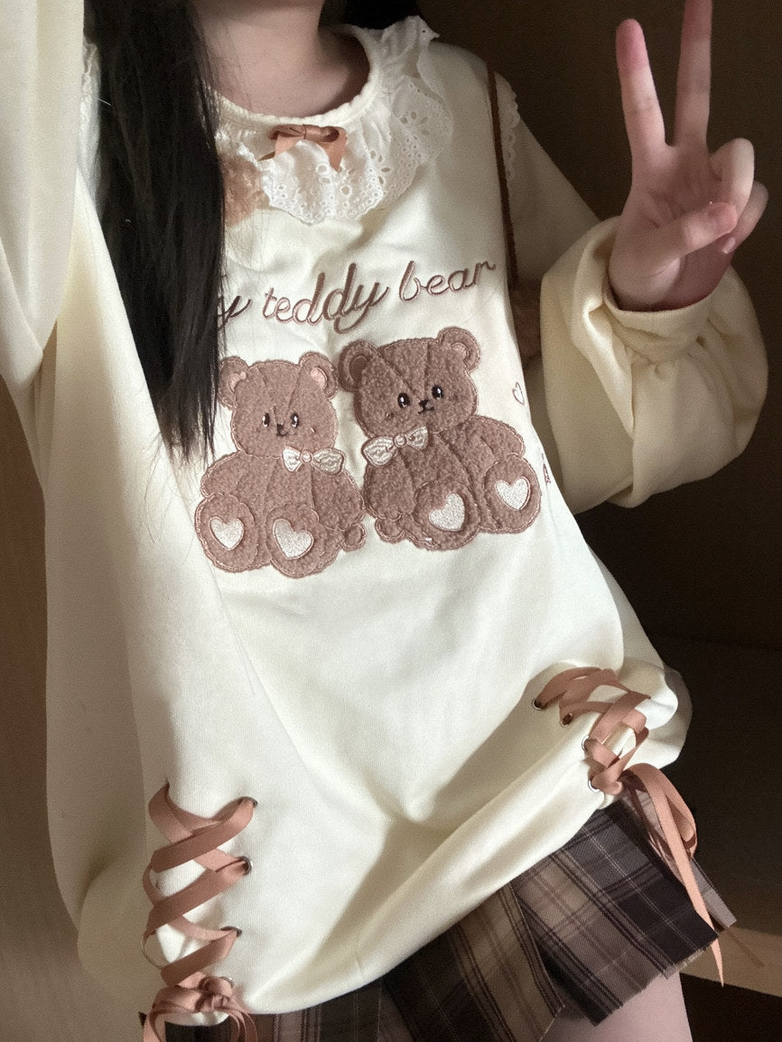 Person wearing a white sweater with teddy bear design and making a peace sign.