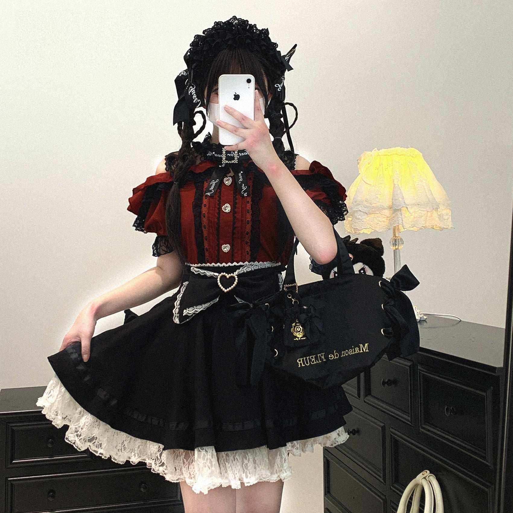 Person wearing a black and red outfit with a matching bag, standing in a room.