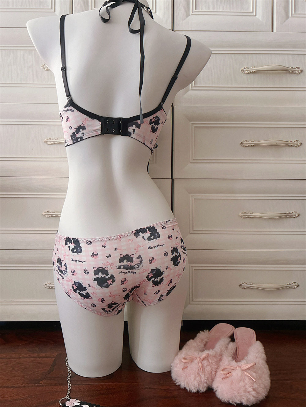 Mannequin wearing a pink and black patterned lingerie set with pink slippers on a wooden floor.