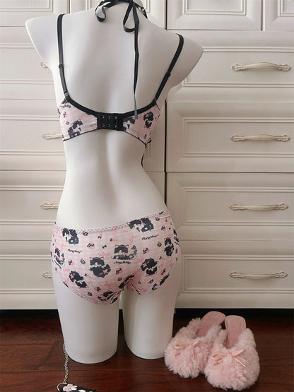Mannequin wearing a pink and black patterned lingerie set with pink slippers on a wooden floor.