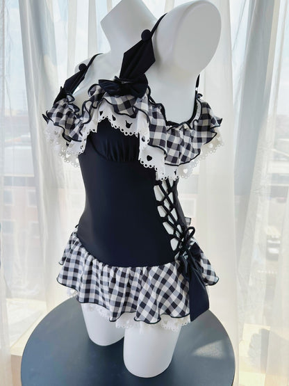Black swimsuit with white ruffles and checkered details on a mannequin against a white curtain background.