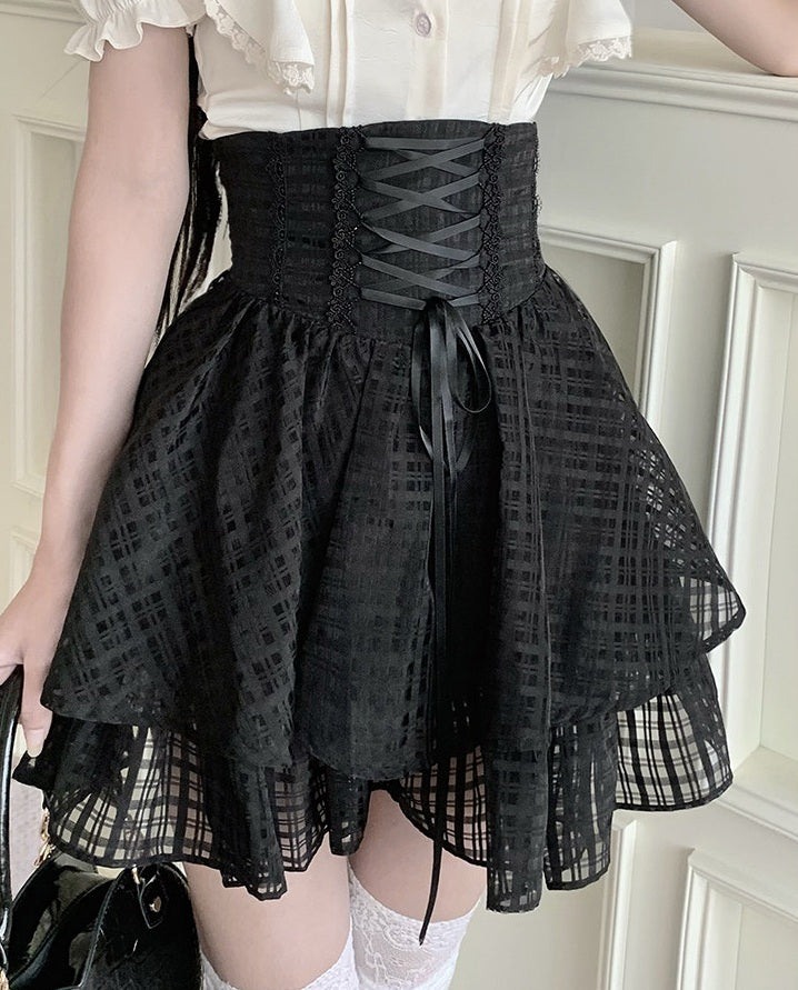 A person wearing a black lace-up corset-style mini skirt with a flared layered skirt and sheer grid-patterned fabric, paired with a white ruffled blouse and white lace socks.