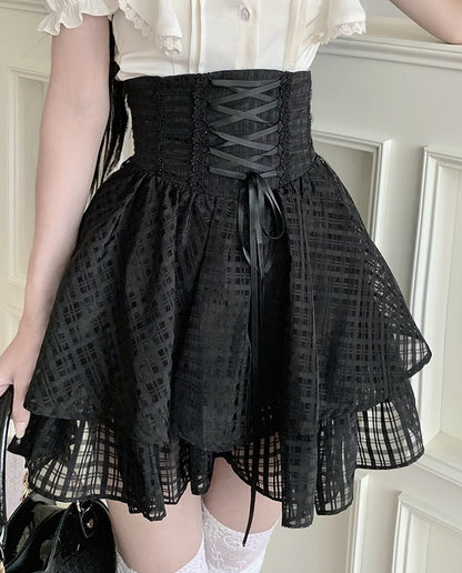 A person wearing a black lace-up corset-style mini skirt with a flared layered skirt and sheer grid-patterned fabric, paired with a white ruffled blouse and white lace socks.