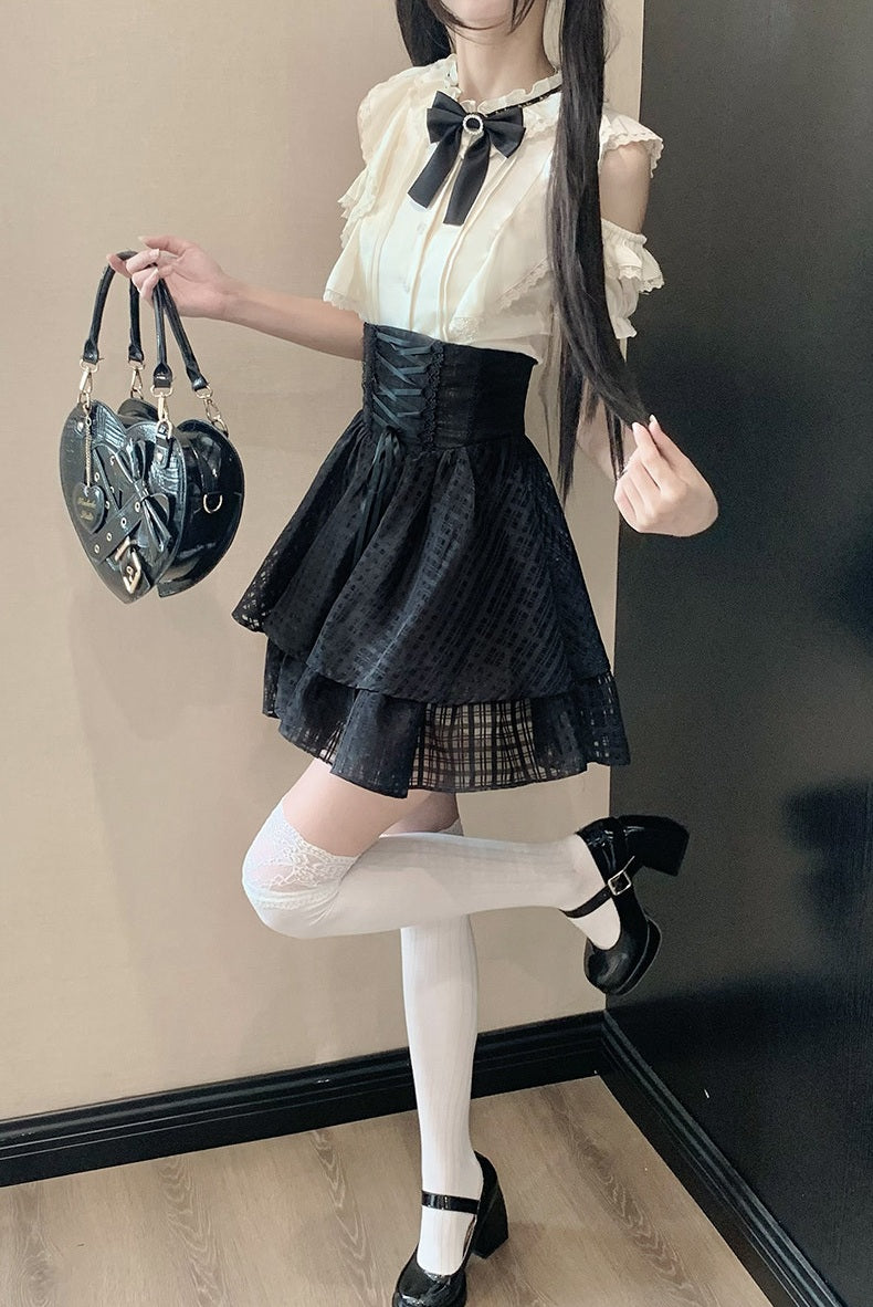 A model wearing a gothic Lolita outfit consisting of a cream ruffled blouse with a black bow, a black pleated mini skirt, white thigh-high stockings, and black Mary Jane shoes, while holding a black heart-shaped handbag.