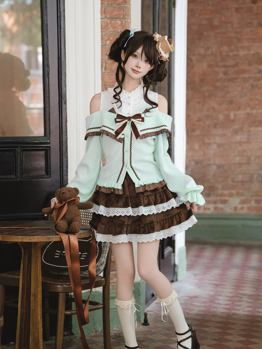 A model wearing a light mint green and brown Lolita-style outfit with lace details, white thigh-high socks, and a small brown teddy bear accessory, standing in front of a brick wall doorway.