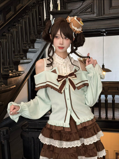 A model wearing a detailed Lolita-style outfit consisting of a pale mint green cardigan with brown trim and a large brown bow, paired with a brown and white ruffled skirt, standing in front of a dark wooden staircase.