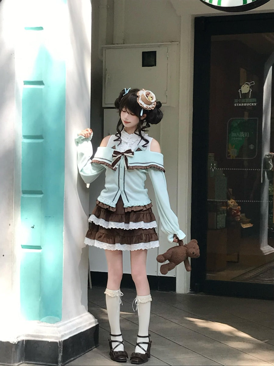 A young woman stands in a doorway wearing a pastel Lolita-style outfit with a light blue off-the-shoulder top, a brown and white ruffled skirt, white knee-high socks, and dark shoes. She holds a small teddy bear and poses beside a brightly lit white pillar.