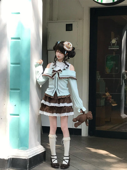 A young woman stands in a doorway wearing a pastel Lolita-style outfit with a light blue off-the-shoulder top, a brown and white ruffled skirt, white knee-high socks, and dark shoes. She holds a small teddy bear and poses beside a brightly lit white pillar.