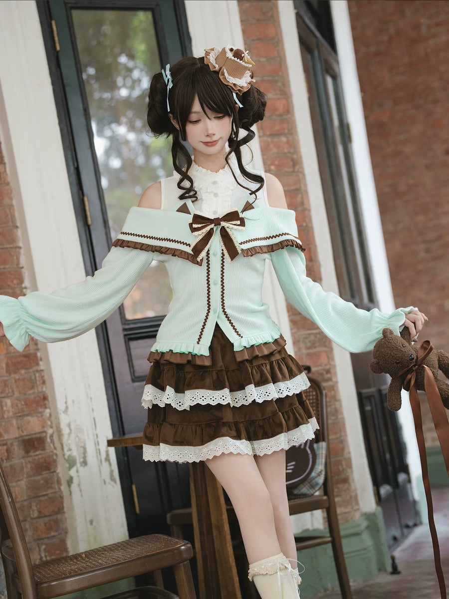 Woman in a light green cardigan and brown skirt standing in front of a brick wall.