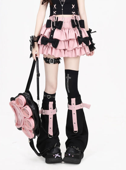 A model wearing a black and pink goth-style outfit, featuring a ruffled pink mini skirt with black bows, black thigh-high socks with pink straps, and a black backpack with pink flower details, set against a plain white background.