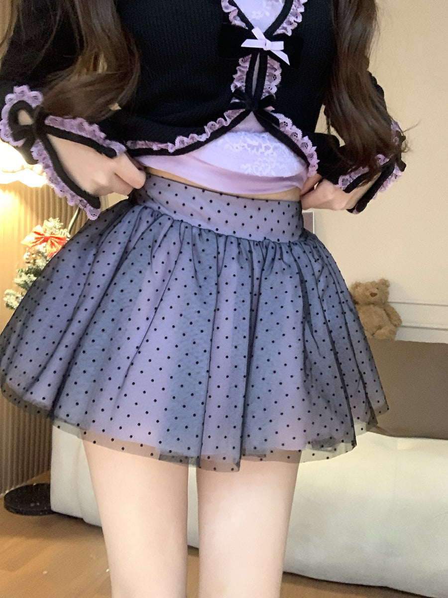 Person wearing a black and white outfit with a polka dot skirt in an indoor setting