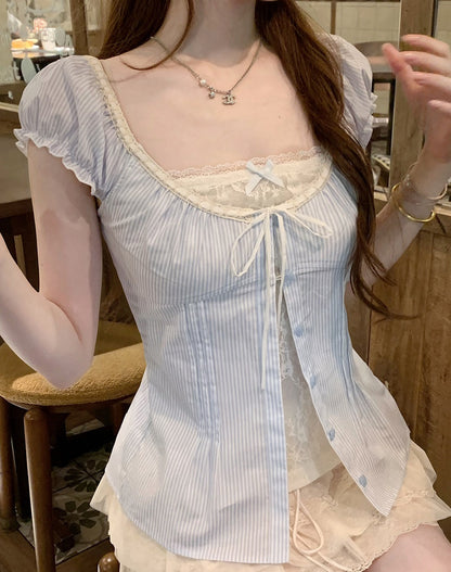 A woman wearing a light blue and white vertically striped camisole top with ruffled sleeves, a square neckline, lace trim, and a front tie closure, paired with a matching light-colored skirt in an indoor setting.