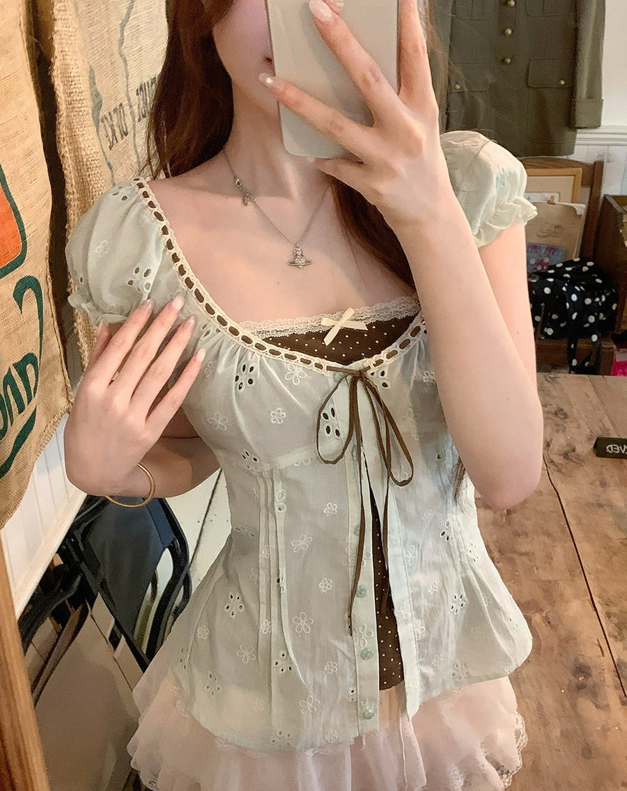 A woman takes a mirror selfie showing a light sage green eyelet top with a brown lace-up trim and a sheer pink tulle skirt, in a rustic indoor setting.