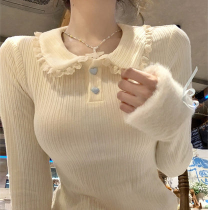 Cream-colored ribbed sweater with ruffled collar and button details worn by a person.