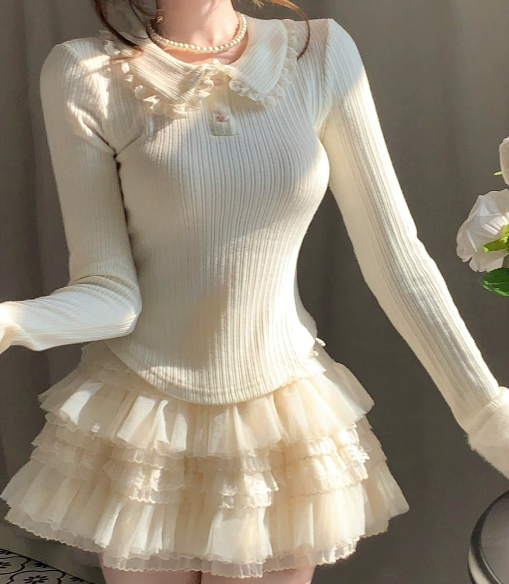 Person wearing a cream-colored dress with long sleeves and a ruffled skirt against a neutral background.