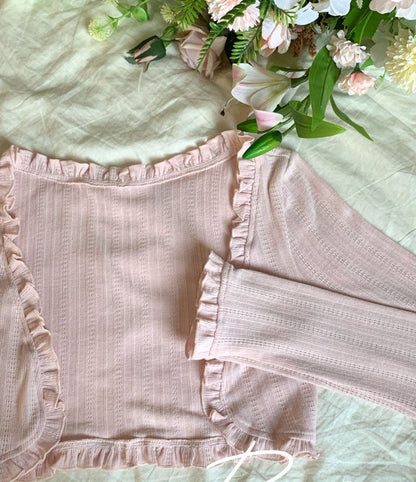 Pink textured cardigan with ruffled edges on a light green background with flowers.