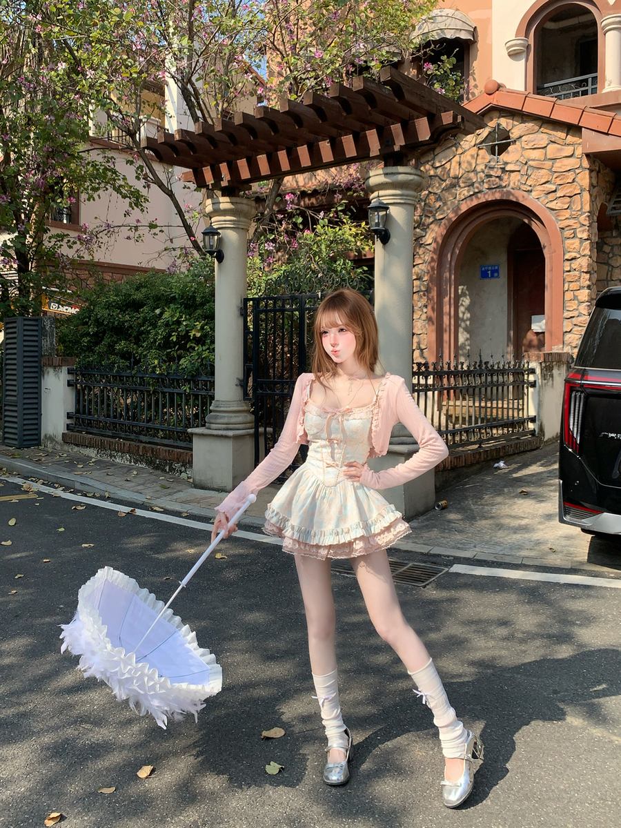 Woman in a white dress holding a white parasol on a street with a building in the background