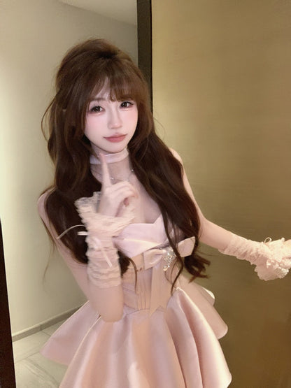 Woman in a light pink dress with sheer sleeves and gloves posing in front of a mirror.