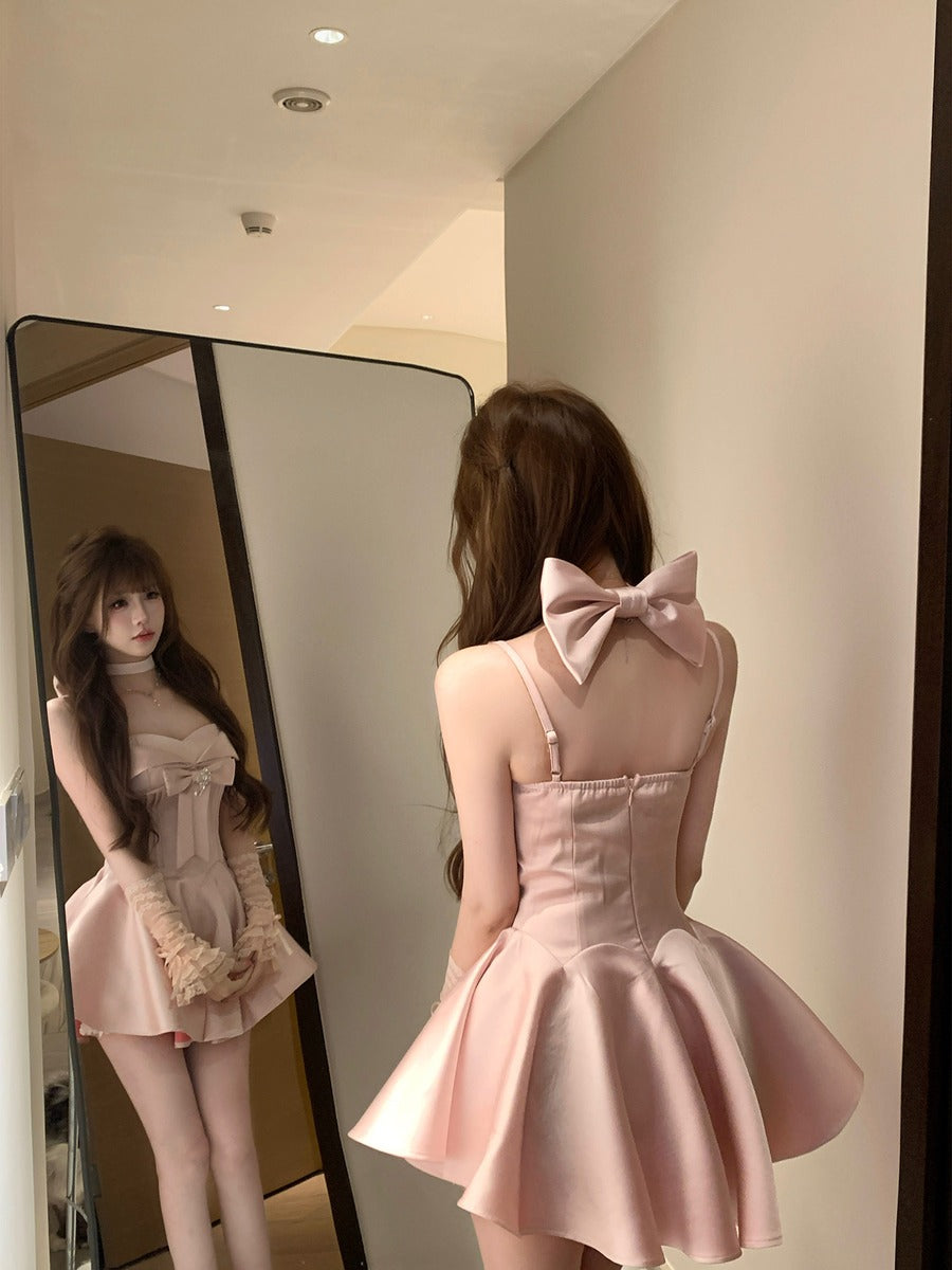 Woman wearing a pink dress with a large bow back, standing in front of a mirror.