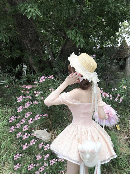 Woman in a pink dress and straw hat standing in a garden with pink flowers and greenery.