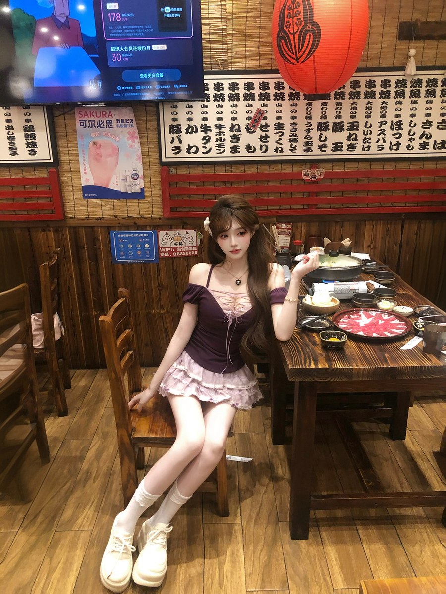 Woman sitting at a table in a restaurant with a TV screen displaying a game in the background.