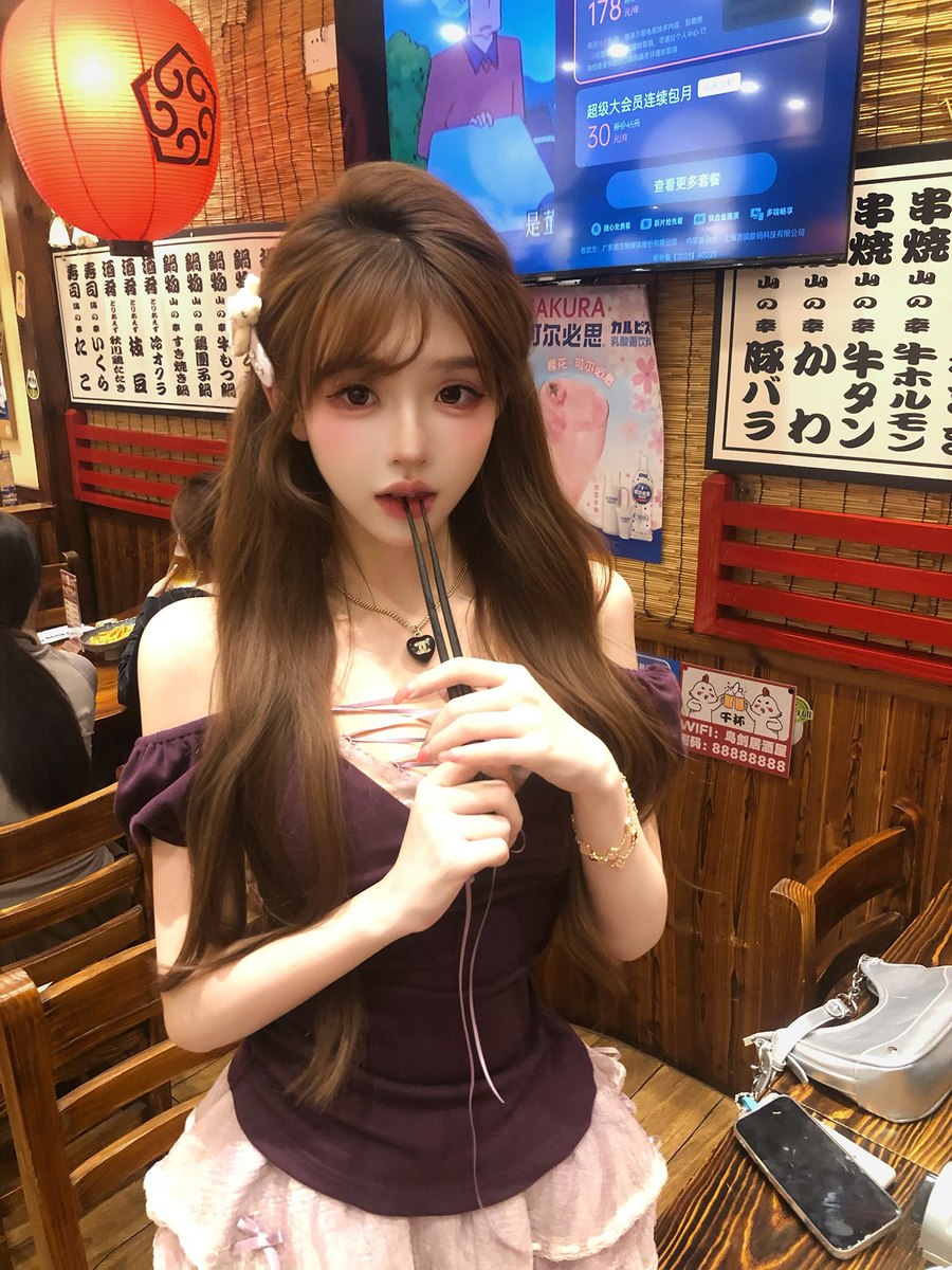 Woman in a restaurant setting holding a straw with a drink, surrounded by decor and a TV screen.