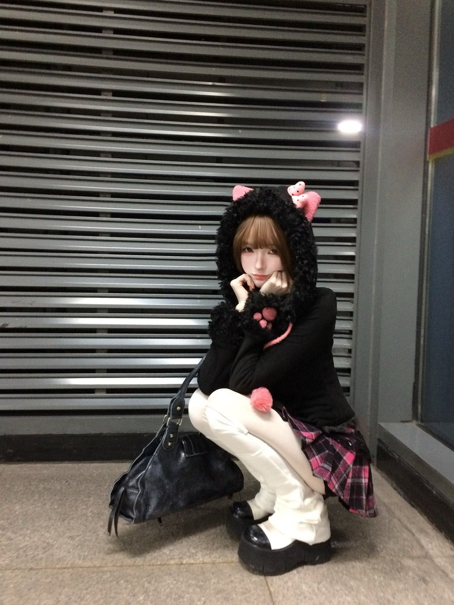 Person wearing a black hoodie with cat ears sitting against a metal shutter.