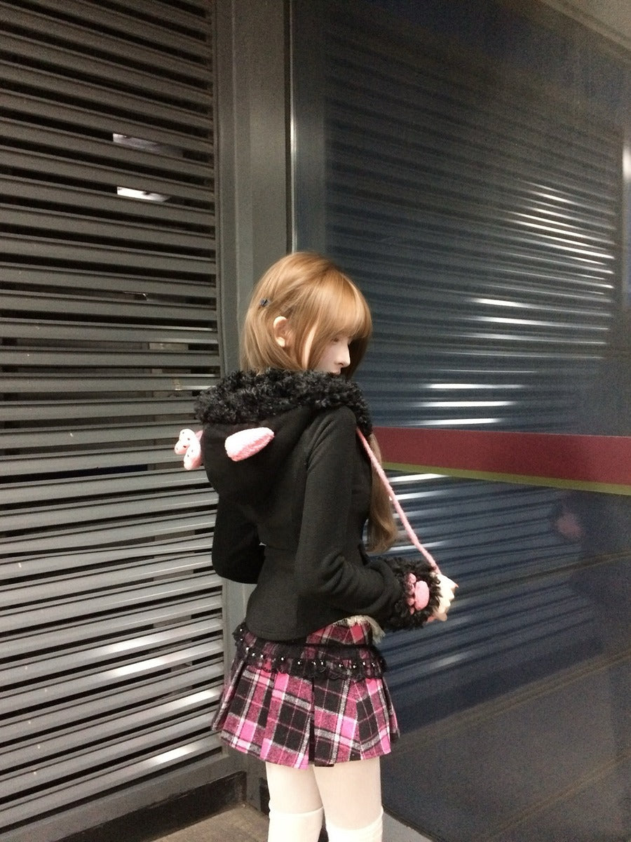 Person wearing a black hoodie with pink accents and a plaid skirt standing in front of a closed shutter.