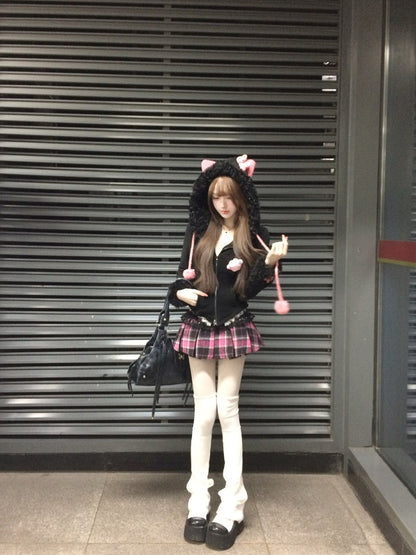 Person wearing a black hoodie with cat ears and a plaid skirt standing in front of a metallic shutter.