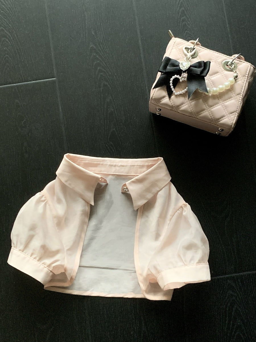 Pet outfit with pink jacket and white pants on a dark surface, next to a small handbag.