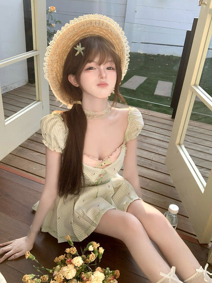 Woman wearing a straw hat and light green dress sitting on a wooden deck.
