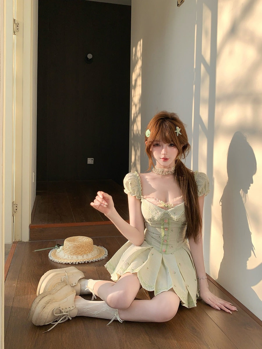 Woman in a vintage-style green dress sitting on a wooden floor with a hat and shoes nearby.