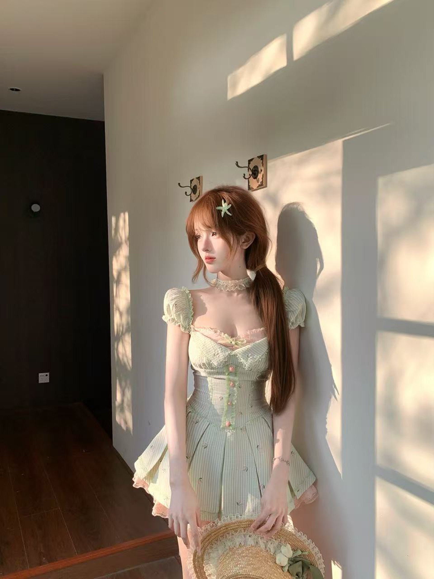 Woman in a light green dress standing in a room with sunlight casting shadows on the wall.