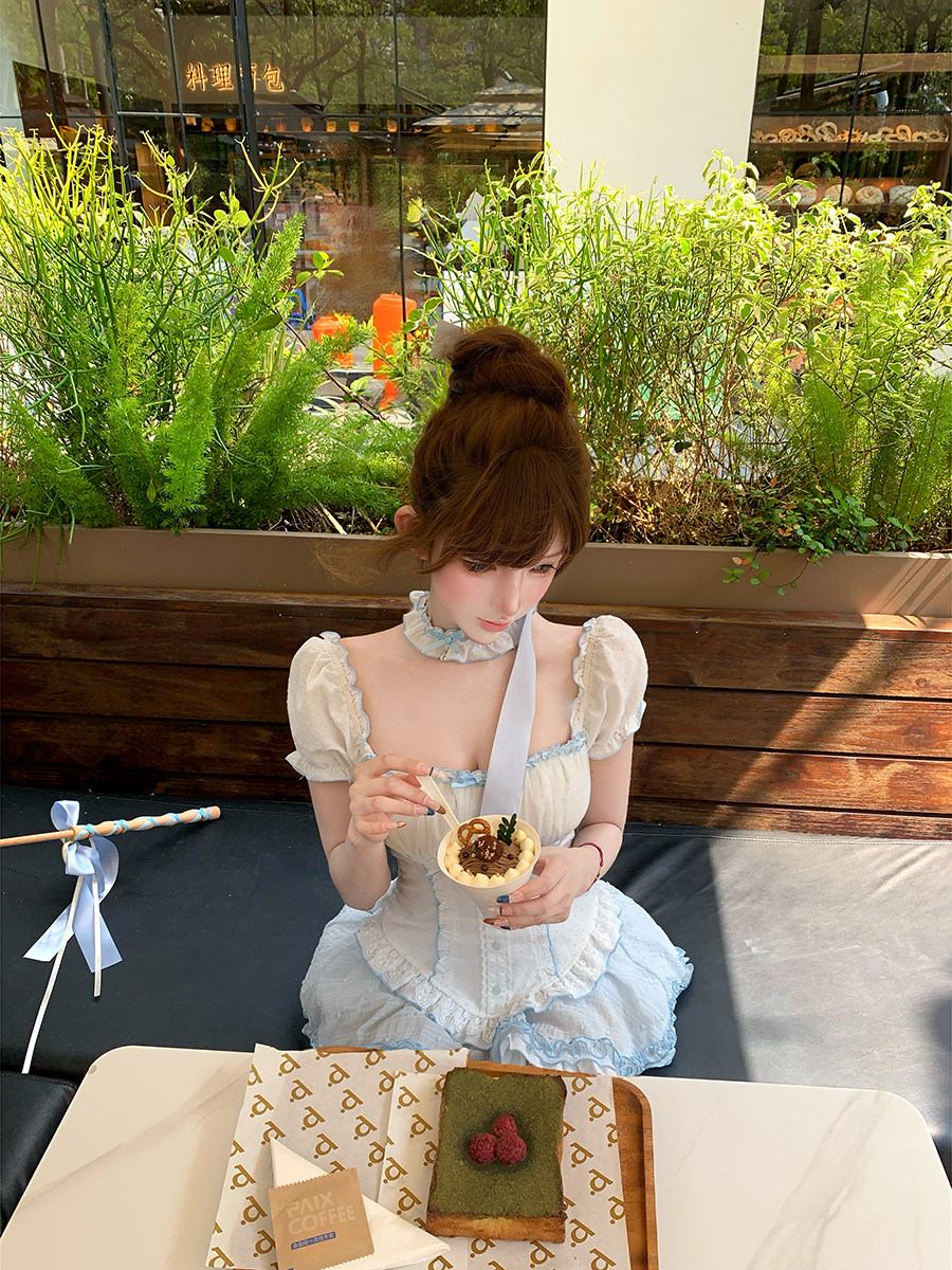 Woman in a white dress sitting outdoors with plants and a table in the background
